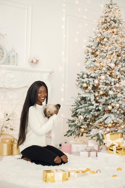 Black girl sitting near Christmas tree holding a little dog