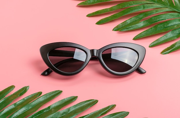 Black glasses and green palm leaves on trendy pink 