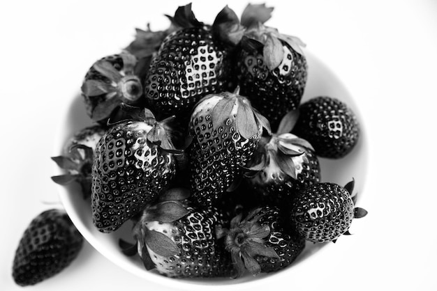 Black glossy strawberries in a white bowl on a white background