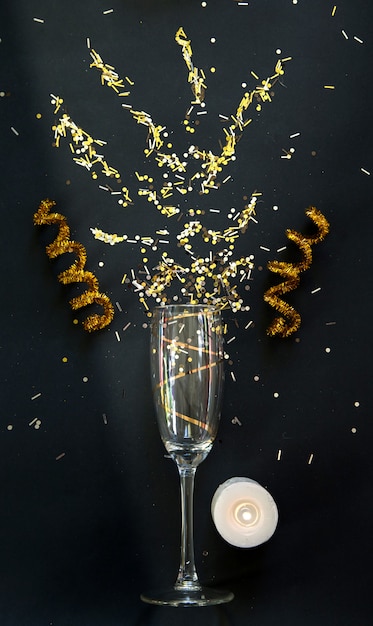 Black and gold  champagne glass and burning candle and confetti 