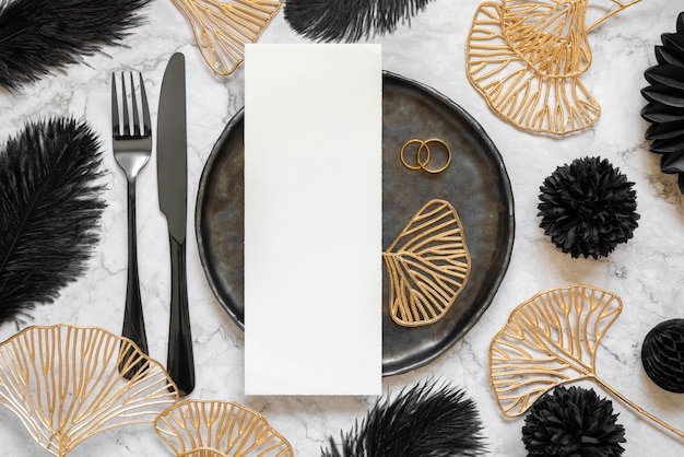 Black and golden wedding table setting with a blank card and rings top view mockup