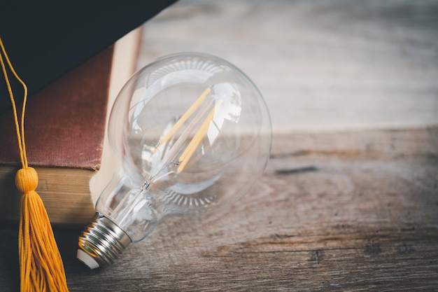 Black graduation hat and book light bulb on wooden table concept ideas graduation