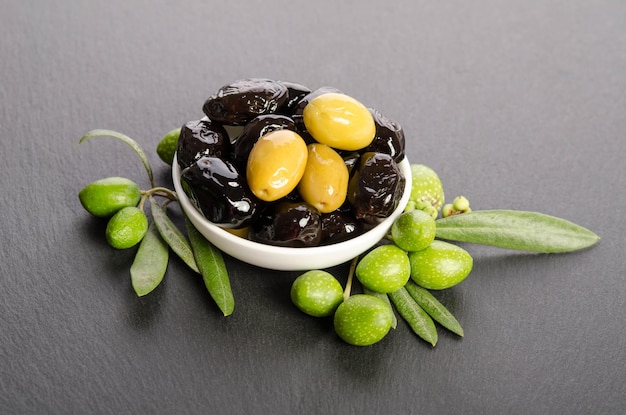 Black and green olives mixed in the porcelain bowl on gray stone