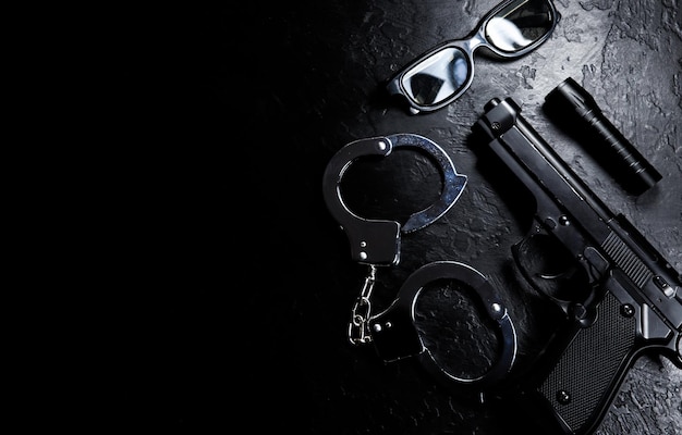 Black gun flashlight glasses and Police metal real handcuffs lie on the black background Private detective work Searching information Crime and robbery prison concept