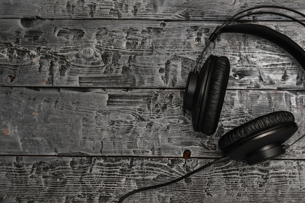 Black headphones with wire on black wooden table.