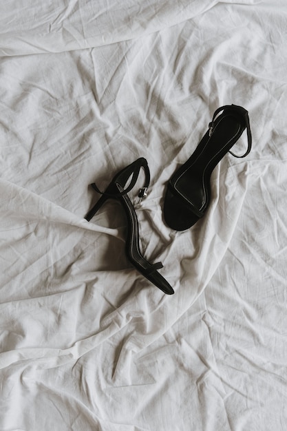 Black high-heel shoes on white crumpled bed linen