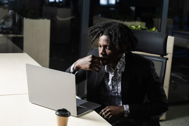 Black IT programmer is working on laptop in coworking space. Handsome african man with laptop in the office.