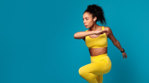 Black lady performing dynamic fitness exercise jumping over blue background