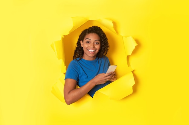 Black Lady Using Phone Looking Through Hole In Torn Paper