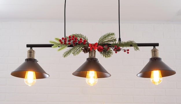 The black lampshade in the industrial loft style is decorated with spruce branches for Christmas and New Year on the background white brick wall Closeup minimalism