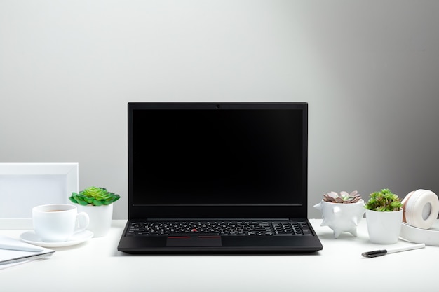 Black laptop with blank display layout template on white background. Office desk workspace in Home interior. White table with laptop for remote work or study.