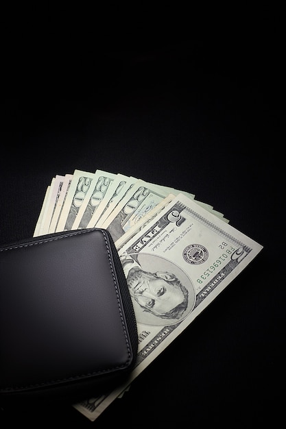 Black leather wallet with cash dollars isolated on a black background