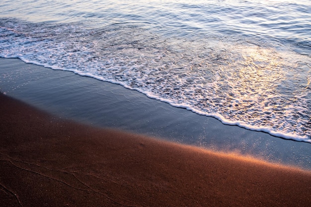 Black magnetite sand and sea waves under sunset rays copper highlights on sand blurred seascape background High quality photo