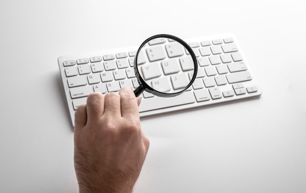 Photo black magnifier on a white keyboard on a white table. business concept.