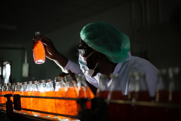 Black male worker inspecting juice bottle on bottling line at a drink factor