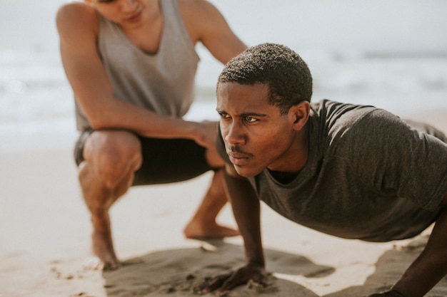 Black man doing pushups with a trainer at the beach