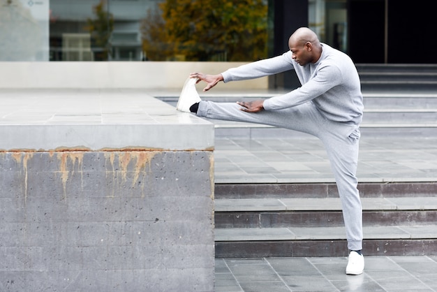 Black man doing stretching before running in urban background