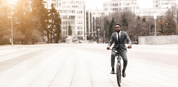 Black man executive is riding his bicycle to the office downtown the setting is lively and