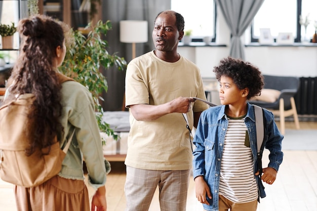 Black man helping his grandson take off backpack while talking to granddaughter