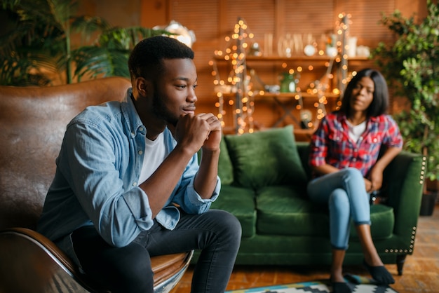 Black man sitting in a comfortable leather chair against his woman on the couch in the living room