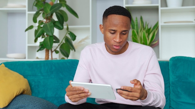 Black man smiles happily makes online purchases using a digital device and makes online Bank payments using a debit or credit card