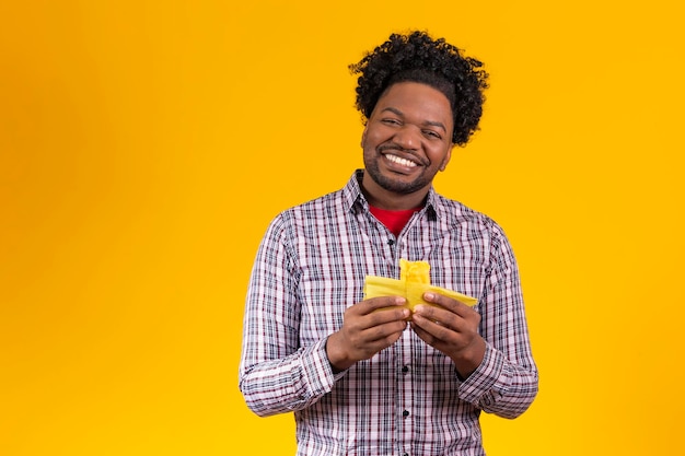 Black man in typical festa junina clothes eating delicious pamonha on yellow background free space for text