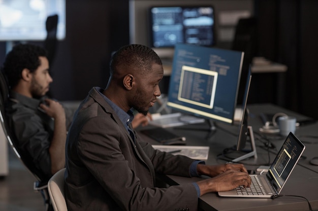 Black man writing code and typing at laptop keyboard