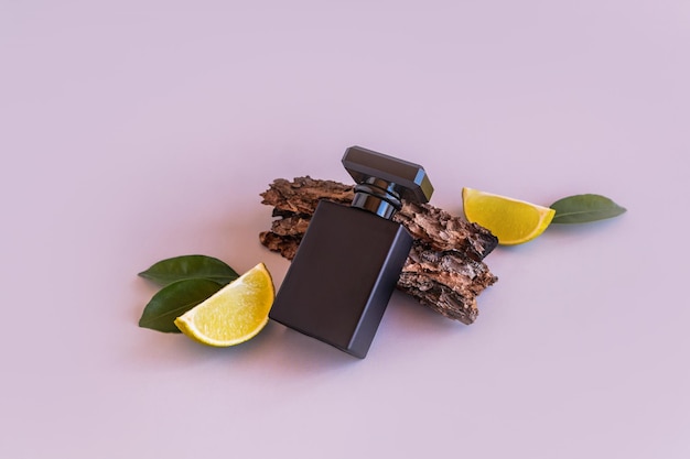 A black matte bottle of men's perfume or toilet water lies on the bark of a tree next to pieces of lime gray background aroma presentation