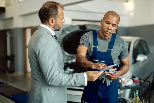 Black mechanic and businessman using digital tablet at auto repair shop