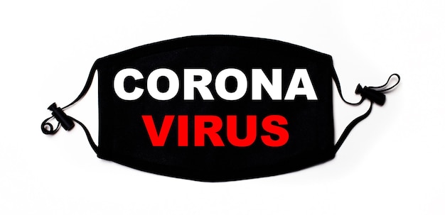 Black medical face mask on a light surface with the inscription CORONA VIRUS. Disease prevention. Medical concept