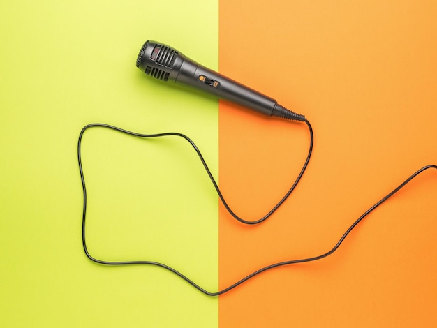 A black microphone with a long wire on a greenorange background The concept of sound recording and music