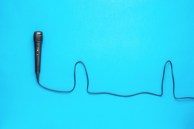 A black microphone with a wire on a blue background The concept of sound recording and music