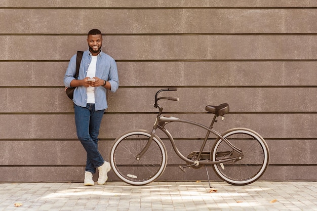 Photo black millennial guy standing next to bike over grey urban wall