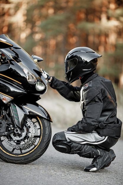 Black motorcyclist in helmet sits near a sports motorcycle and puts his hand on it