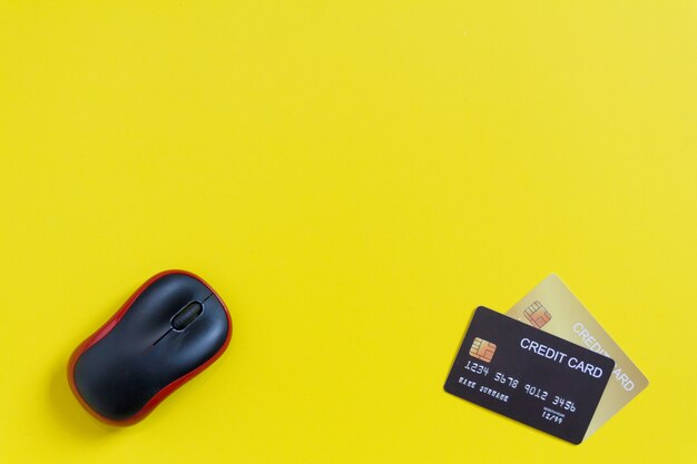 Black mouse with credits cards on yellow paper background