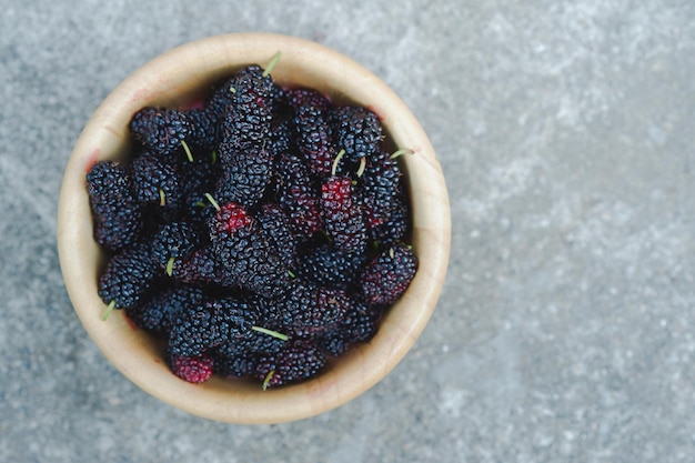 Black mulberry in wooden cup on cement floor It is a healthy berry with a sweet and sour taste