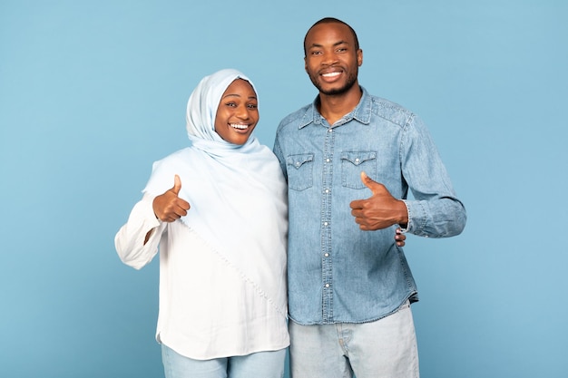 Black Muslim Couple Gesturing Thumbs Up In Approval Blue Background