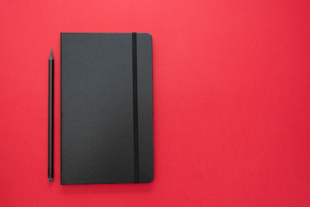 Black notebook on red background. Top view of working table, work space. abstract business flat lay.