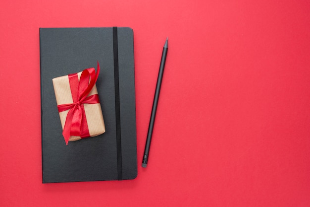 Black notebook on red background with a gift box. Valentine's Day concept.