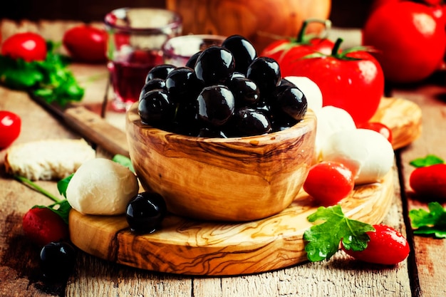 Black olives in a vintage wooden bowl goat cheese tomatoes and wine Still Life with appetizers rustic style selective focus