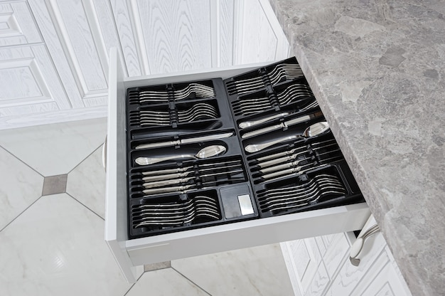 Black open drawer with silver cutlery in modern white kitchen