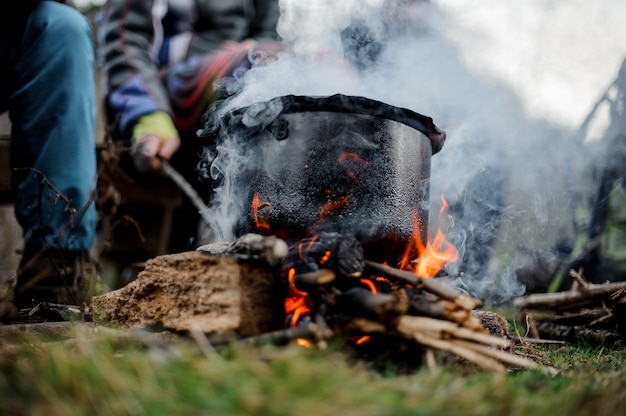 Black pan with a dish standing on the bonfire over the group of people