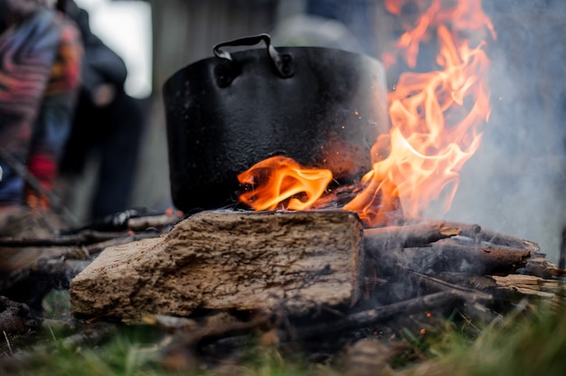 Black pan with a dish standing on the campfire over the group of people