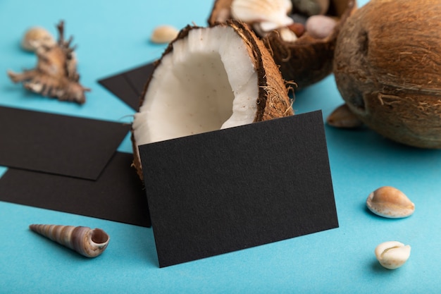 black paper business card with coconut and seashells on blue background. side view, copy space.