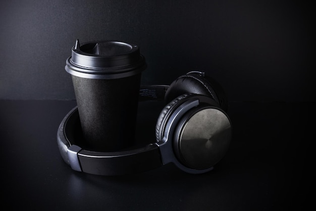 Black paper disposable cup and wireless headphones on dark background