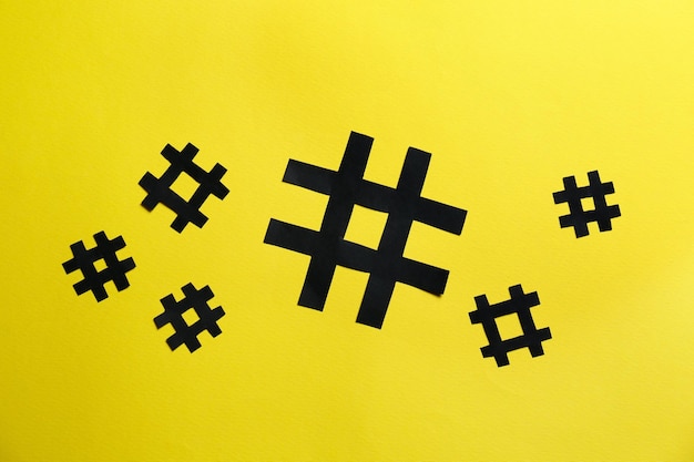 Black paper hashtag symbols on yellow background flat lay