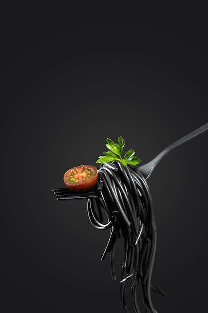 Black pasta rolled on a fork isolated on black background   with copyspace. Vertical format. Cooking concept.