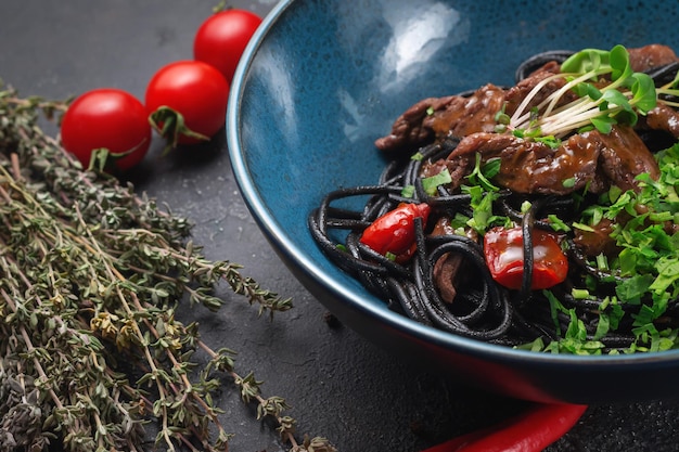 Black pasta with beef and sun-dried tomatoes in a blue plate on a dark stone table