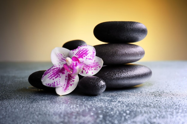 Black pebbles with orchid on grey table close up