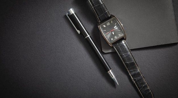 Black pen wristwatch notepad on the black background